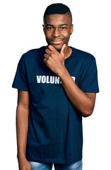 Young african american man wearing volunteer t shirt looking confident at the camera smiling with crossed arms and hand raised on chin. thinking positive.