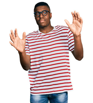Young african american man wearing casual t shirt and glasses afraid and terrified with fear expression stop gesture with hands, shouting in shock. panic concept.