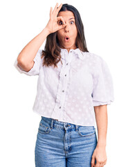 Fototapeta premium Young beautiful brunette woman wearing casual shirt doing ok gesture shocked with surprised face, eye looking through fingers. unbelieving expression.