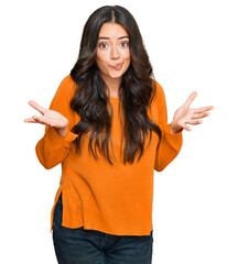Beautiful brunette young woman wearing casual orange sweater clueless and confused expression with...