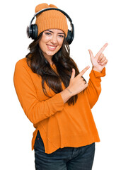 Beautiful brunette young woman listening to music using headphones smiling and looking at the camera pointing with two hands and fingers to the side.