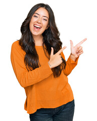 Beautiful brunette young woman wearing casual orange sweater smiling and looking at the camera pointing with two hands and fingers to the side.