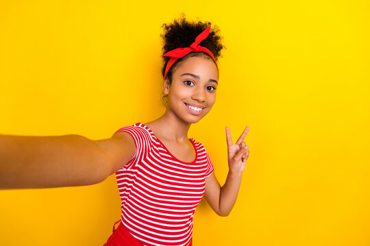 Photo of positive pretty lady wear striped red t-shirt recording video vlog showing v-sign isolated yellow color background