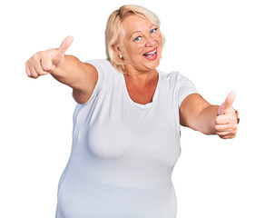 Middle age blonde woman wearing casual white t shirt approving doing positive gesture with hand, thumbs up smiling and happy for success. winner gesture.