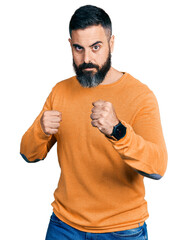Hispanic man with beard wearing casual winter sweater ready to fight with fist defense gesture,...