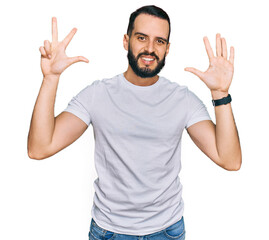 Young man with beard wearing casual white t shirt showing and pointing up with fingers number eight while smiling confident and happy.