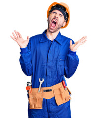 Young hispanic man wearing worker uniform celebrating mad and crazy for success with arms raised and closed eyes screaming excited. winner concept