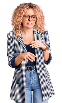 Young blonde woman with curly hair wearing business jacket and glasses disgusted expression, displeased and fearful doing disgust face because aversion reaction.