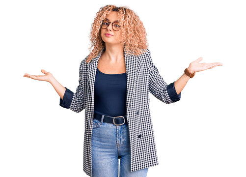 Young blonde woman with curly hair wearing business jacket and glasses clueless and confused expression with arms and hands raised. doubt concept.