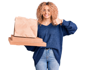 Young blonde woman with curly hair holding delivery food smiling happy and positive, thumb up doing excellent and approval sign