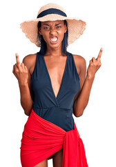 Young african american woman wearing swimsuit and summer hat showing middle finger doing fuck you bad expression, provocation and rude attitude. screaming excited