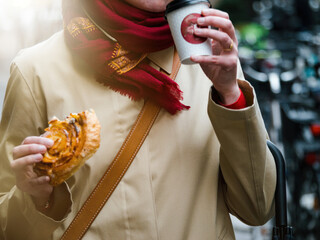In the rain, an adult woman holds a cup of coffee, finding comfort in the moment despite the...