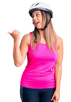 Young beautiful woman wearing bike helmet smiling with happy face looking and pointing to the side with thumb up.