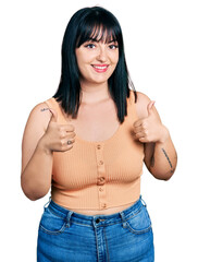 Young hispanic plus size woman wearing casual clothes success sign doing positive gesture with hand, thumbs up smiling and happy. cheerful expression and winner gesture.