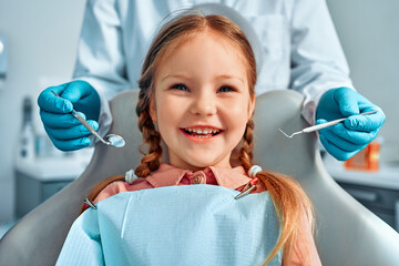 Cropped portrait of girl with pigtails hair sitting in dental chair looking at camera and smiling....