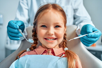 Cropped portrait of little girl with pigtails hair sitting in dental chair looking at camera and...