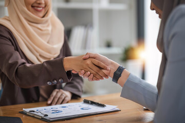 A beautiful and cheerful Asian Muslim businesswoman shaking hands with a female business partner...