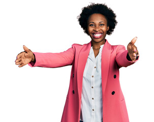 African american woman with afro hair wearing business jacket looking at the camera smiling with open arms for hug. cheerful expression embracing happiness.