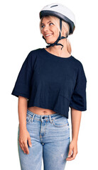 Young beautiful blonde woman wearing bike helmet looking away to side with smile on face, natural expression. laughing confident.