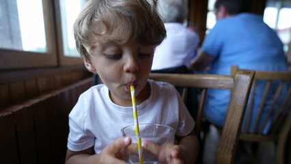 Little boy drinking refreshment beverage using straw at restaurant