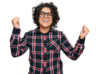 Young hispanic woman with curly hair wearing casual clothes and glasses screaming proud, celebrating victory and success very excited with raised arms