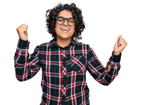 Young hispanic woman with curly hair wearing casual clothes and glasses screaming proud, celebrating victory and success very excited with raised arms