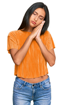 Young brunette arab woman wearing casual clothes sleeping tired dreaming and posing with hands together while smiling with closed eyes.