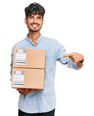 Young hispanic man holding delivery package smiling happy pointing with hand and finger