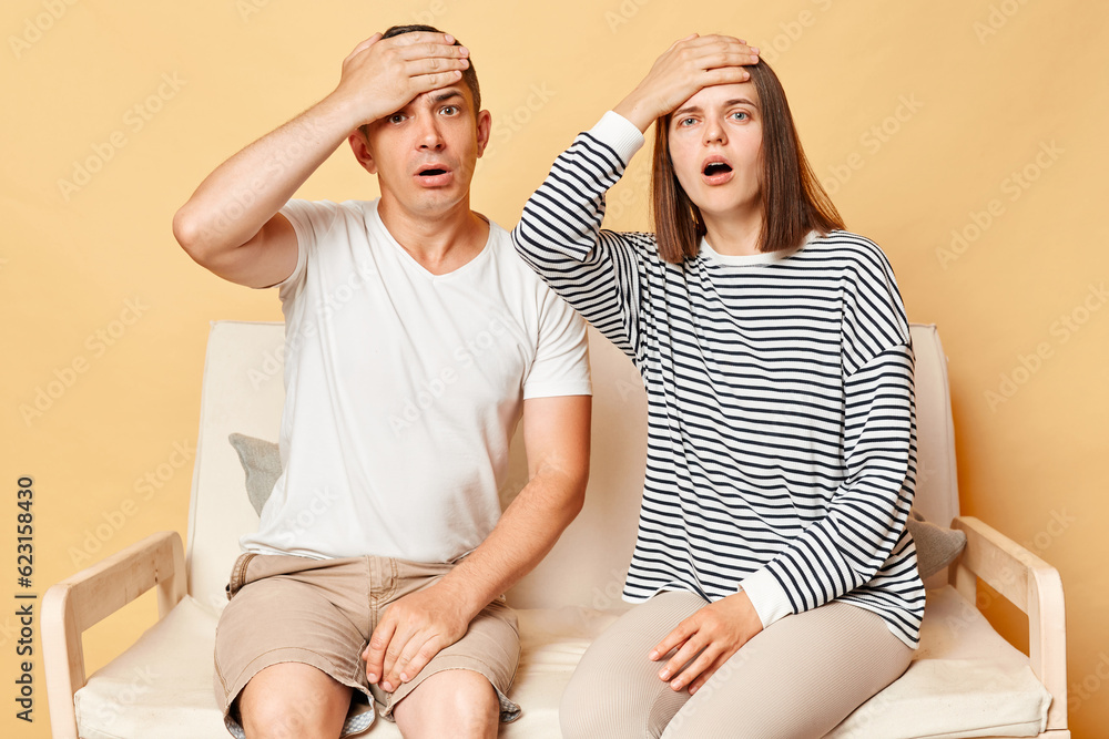 Wall mural Shocked woman and man dressedcasuallysitting on sofa isolated over beige background being stressed and felling unhappy having problems, astonished of troubles.