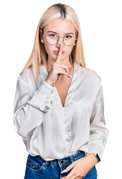 Beautiful blonde woman wearing elegant shirt and glasses asking to be quiet with finger on lips. silence and secret concept.