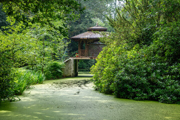 a wooden house in a park on a bridge above the water in a green landscape
