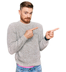 Young redhead man wearing casual winter sweater pointing aside worried and nervous with both hands,...