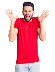 Fototapeta premium Young handsome man with beard wearing casual t-shirt celebrating mad and crazy for success with arms raised and closed eyes screaming excited. winner concept