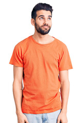 Fototapeta premium Young handsome man with beard wearing casual t-shirt smiling looking to the side and staring away thinking.