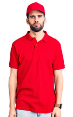 Young handsome man with beard wearing delivery uniform looking sleepy and tired, exhausted for fatigue and hangover, lazy eyes in the morning.