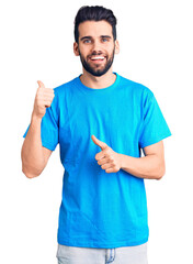 Young handsome man with beard wearing casual t-shirt pointing to the back behind with hand and thumbs up, smiling confident