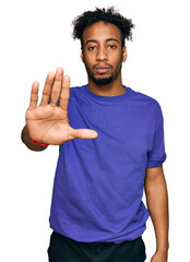 Young african american man with beard wearing casual purple t shirt doing stop sing with palm of the hand. warning expression with negative and serious gesture on the face.