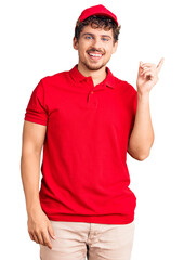 Young handsome man with curly hair wearing delivery uniform smiling happy pointing with hand and finger to the side