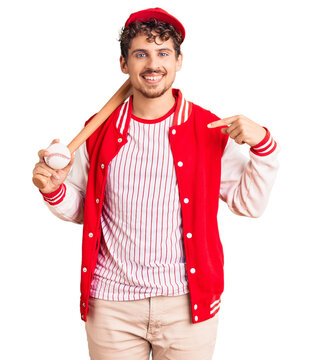 Young handsome man with curly hair playing baseball holding bat and ball pointing finger to one self smiling happy and proud