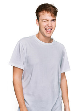 Young caucasian man wearing casual white t shirt winking looking at the camera with sexy expression, cheerful and happy face.