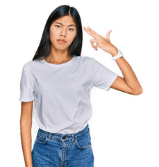 Beautiful young asian woman wearing casual white t shirt shooting and killing oneself pointing hand and fingers to head like gun, suicide gesture.