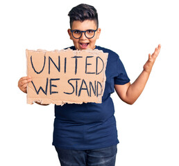 Little boy kid holding united we stand banner celebrating victory with happy smile and winner expression with raised hands