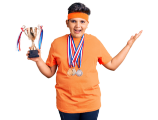 Little boy kid holding champion trophy and wearing medals celebrating victory with happy smile and winner expression with raised hands