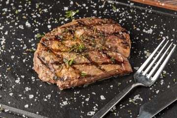 Grilled ribeye steak with rosemary and thyme on stone cutting board