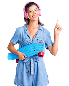 Young beautiful woman wearing headphones and holding skate surprised with an idea or question pointing finger with happy face, number one