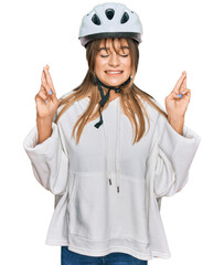 Teenager caucasian girl wearing bike helmet gesturing finger crossed smiling with hope and eyes closed. luck and superstitious concept.