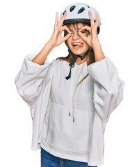 Teenager caucasian girl wearing bike helmet doing ok gesture like binoculars sticking tongue out, eyes looking through fingers. crazy expression.