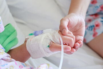 Mother holding child hand with saline IV solution in hospital