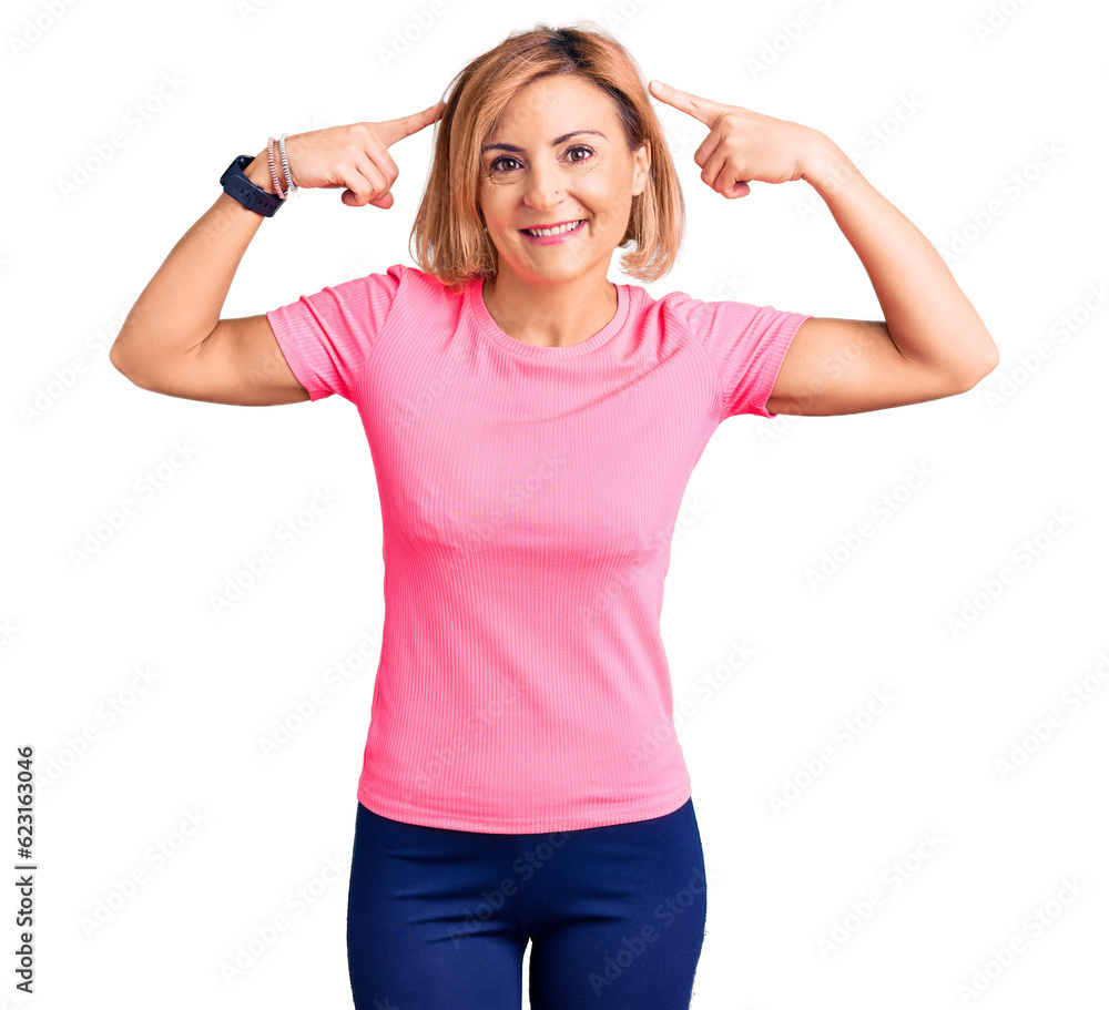 Sticker young blonde woman wearing sportswear smiling pointing to head with both hands finger, great idea or