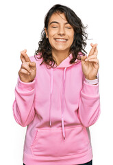 Obraz na płótnie Canvas Young hispanic woman wearing casual sweatshirt gesturing finger crossed smiling with hope and eyes closed. luck and superstitious concept.
